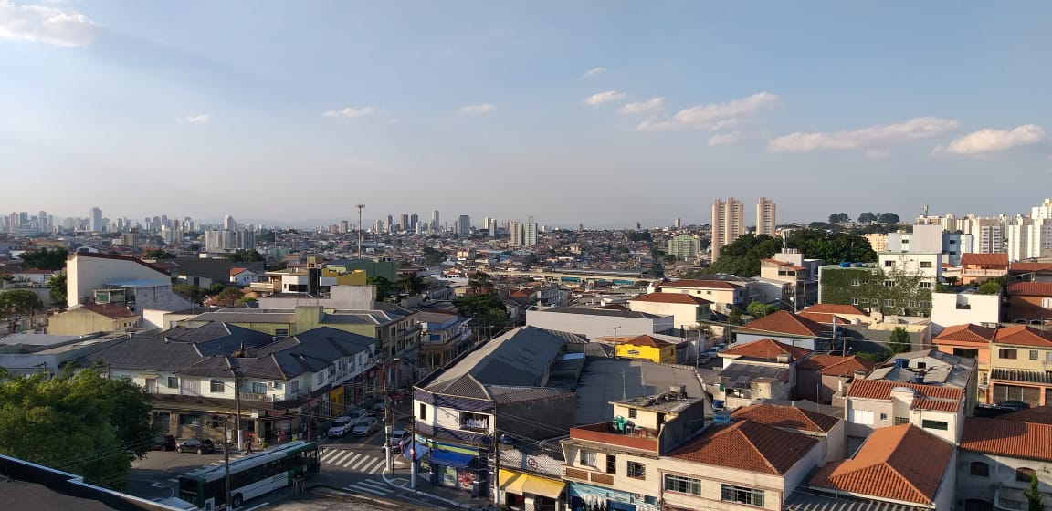 Foto aérea mostra o bairro de São Lucas, com suas casas e prédios, com um céu azul e nuvens ao fundo